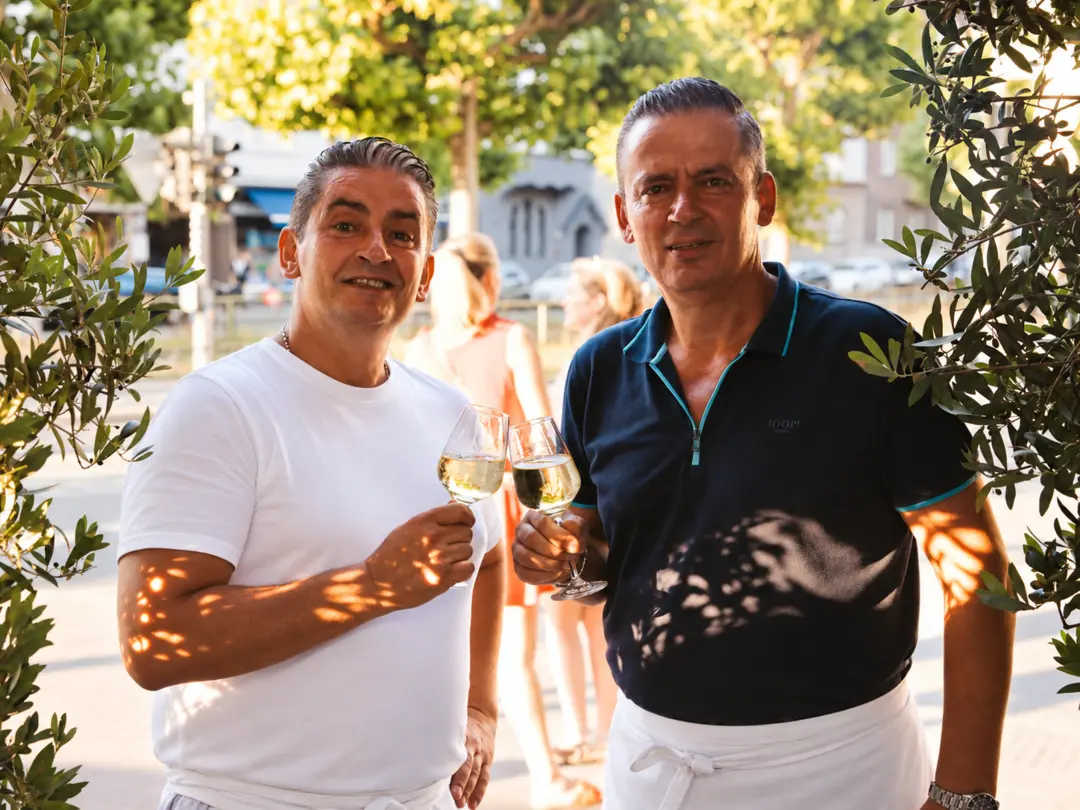 Die Gastgeber der Pizzeria Fratelli stoßen mit Weißwein vor dem Restaurant an