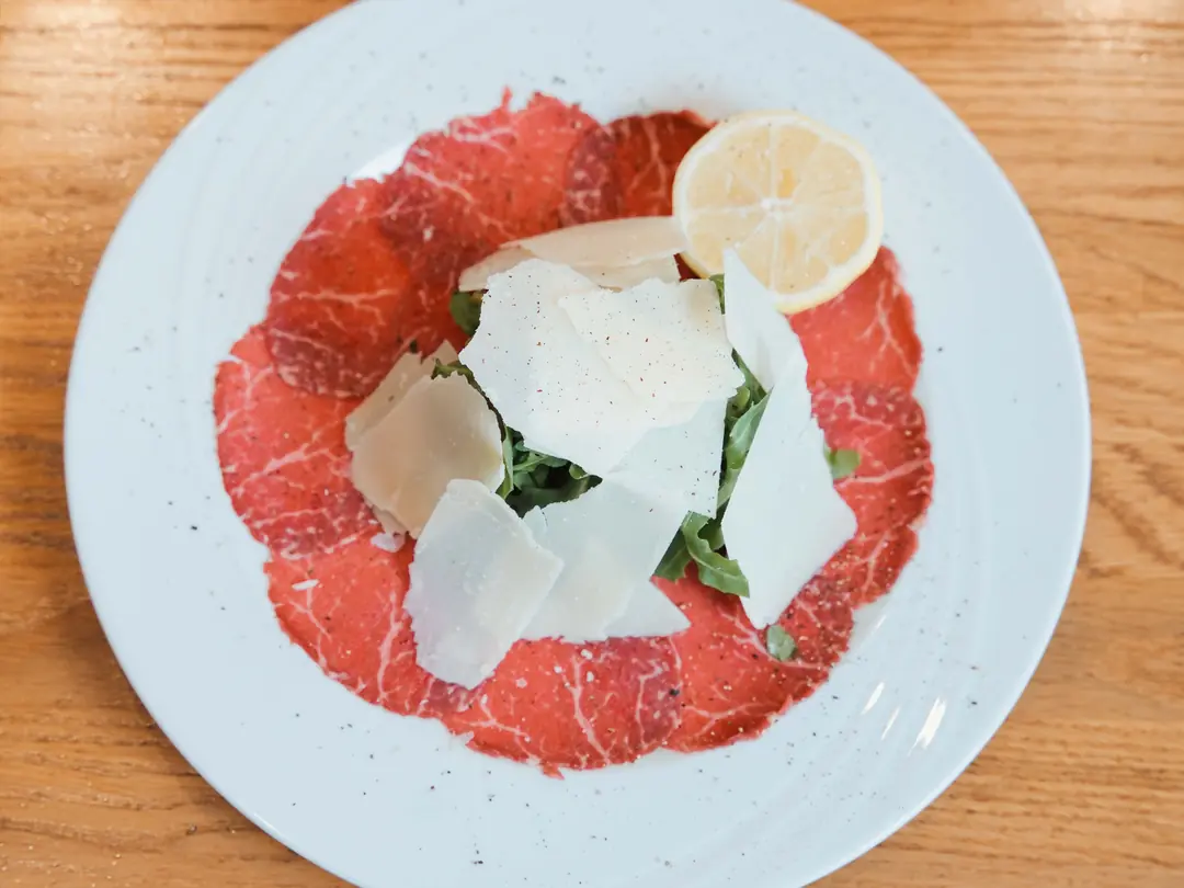 Carpaccio mit Rucola, Parmesan und Zitrone auf einem weißen Teller