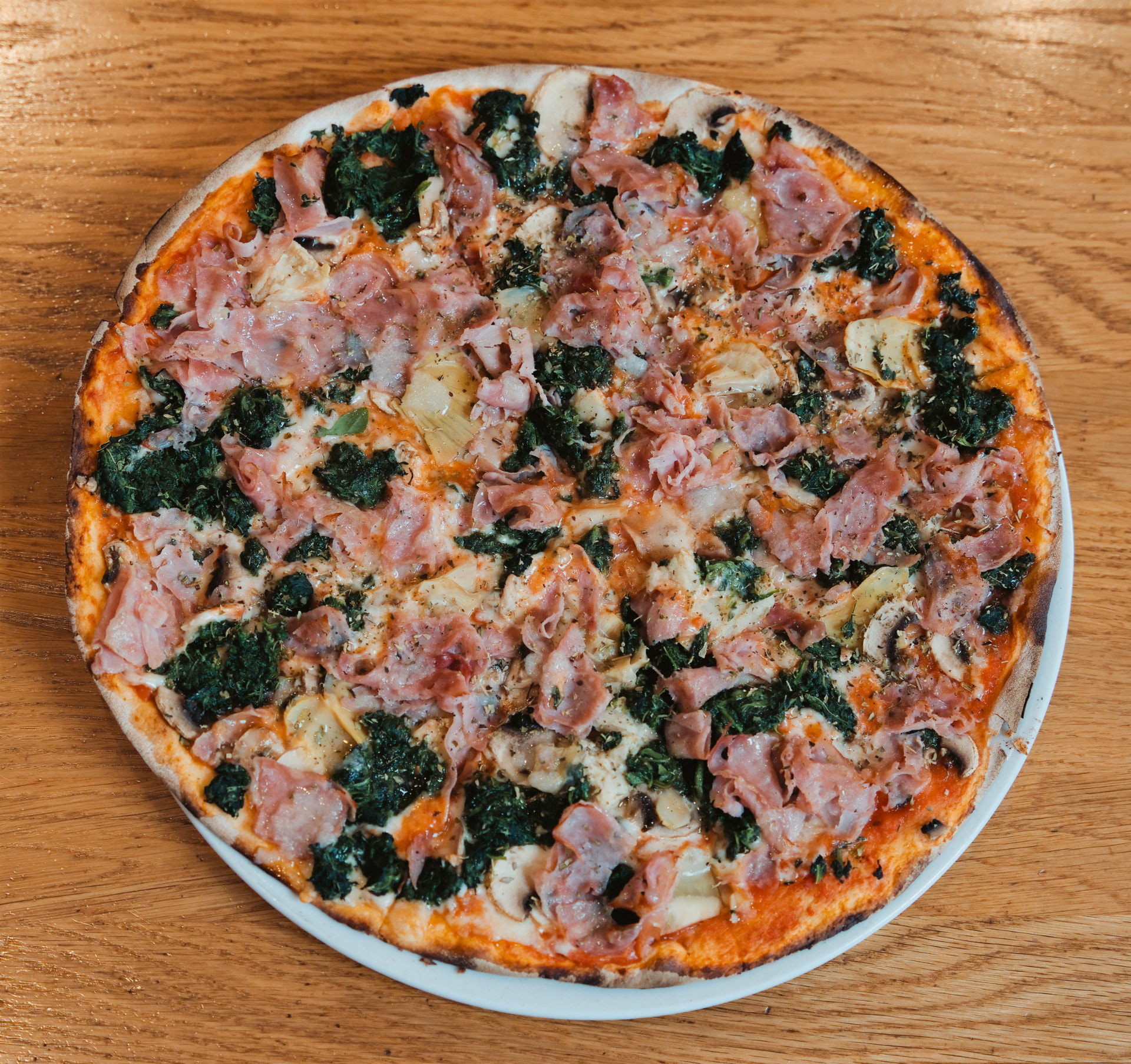 Frisch gebackene Pizza mit Schinken, Spinat, Pilzen und Artischocken auf Holztisch