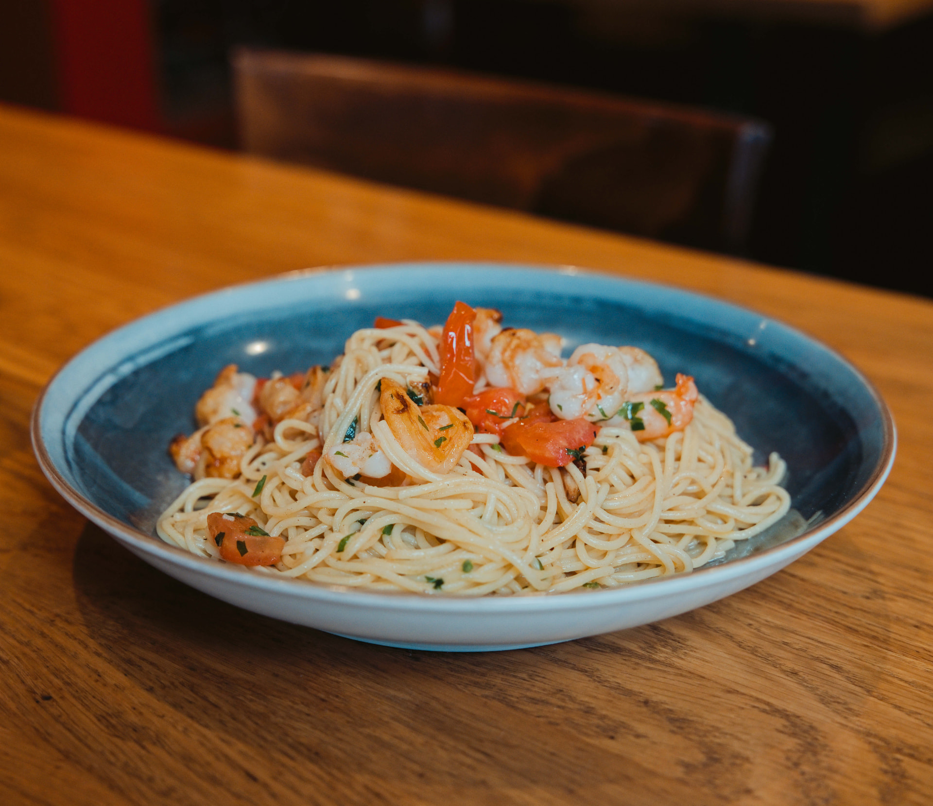 Spaghetti mit Garnelen, Knoblauch und Tomaten in einer blauen Keramikschale